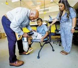  ?? NELVIN C. CEPEDA U-T PHOTOS ?? Herb Barrack, chief medical officer at Limber, helps Jonah Villamil, with his mother Rhodalyn Villamil, put on his new 3D printed prosthetic limb.