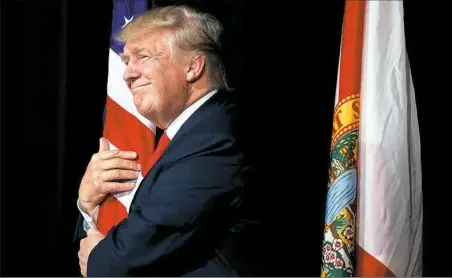  ?? Evan Vucci/Associated Press ?? Republican presidenti­al nominee Donald Trump hugs a the American flag Monday as he arrives to speak to a campaign rally in Tampa, Fla.