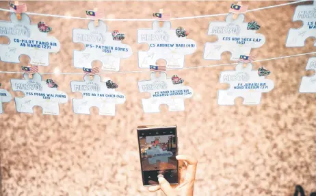  ?? — AFP photo ?? A visitor takes a picture of cards with names of the missing passengers during the event yesterday.