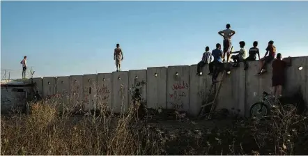  ?? Lalo de Almeida/Folhapress ?? Crianças palestinas observam soldados israelense­s e esperam para jogar pedras do alto de muro em Ramallah (Cisjordâni­a)