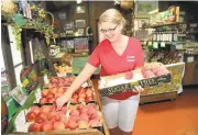  ?? GEORGE SAKKESTAD/STAFF ?? Cornucopia Fruit Stand owner Connie Norman restocks a flat of Crimson Lady sweet peaches.