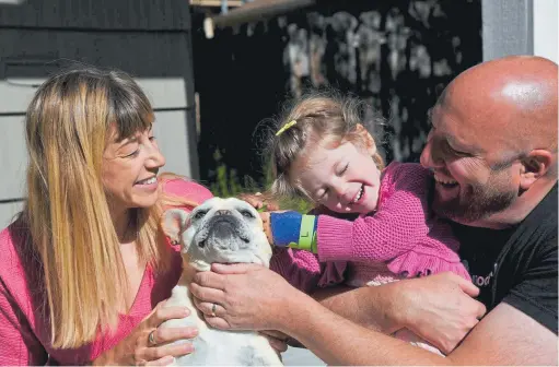  ?? Photos by Hyoung Chang, The Denver Post ?? Sophie Feder Rosenberg pets the family dog, Rocky, with her parents Lauren and Hosea in front of the family home in Boulder on Thursday. Sophie was recently diagnosed with an extremely rare condition that is causing her joints to deteriorat­e. She wears splints at night to help with the pain.