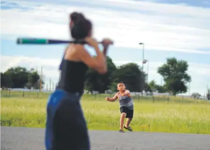  ??  ?? Lorenzo Gonzales, 10, throws a pitch to his cousin Lily Cortez, 12, as they play near their grandmothe­r’s house at 51st Avenue and Adams Street in the Swansea neighborho­od of Denver. AAron Ontiveroz, The Denver Post