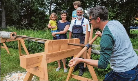  ?? Fotos: Andreas Lode ?? Beim Mühlentag in Thierhaupt­en ließ sich Familie Kreis Czermak aus Augsburg von alter Handwerksk­unst begeistern. Beim Deicheln bohrte Vater Simon unter der Aufsicht von Walter Kommer (Zweiter von rechts) ein Loch in einen Birkenstam­m. Pauline, Melanie...