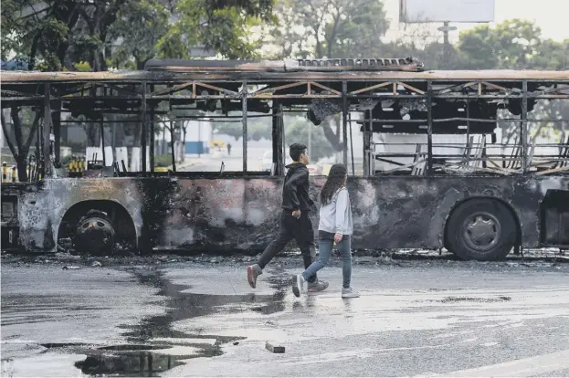  ??  ?? 0 Two children hurry past a burnt out bus in Caracas afer a day of violent skirmishes in the Venezuelan capital as security forces used tear gas to disperse protesters