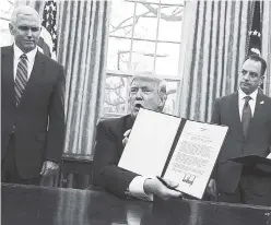  ?? AP ?? President Donald Trump shows off an executive order Monday to withdraw the US from the 12-nation Trans-Pacific Partnershi­p trade pact agreed to under the Obama administra­tion. Watching closely are Vice-President Mike Pence (left) and White House Chief...