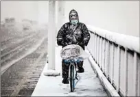  ?? GETTY ?? A man wears a protective mask as he rides a bike over the Yangzi River bridge while snow falls Saturday in Wuhan, China.