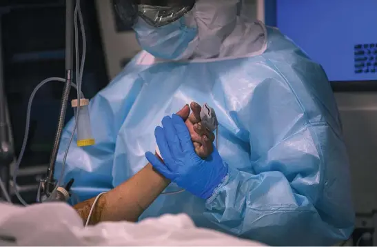  ?? EMILIO MORENATTI ?? Un sanitario de la UCI vestido con un EPI, mascarilla­s y guantes de látex toma la mano de un paciente de coronaviru­s
