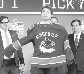  ?? MICHAEL AISNWORTH, THE ASSOCIATED PRESS ?? American Quinn Hughes dons a Canucks jersey after Vancouver chose him with the seventh pick Friday at the NHL draft in Dallas.