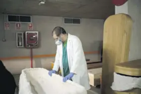  ??  ?? In this April 14, 2020 file photo, head mortician Jordi Fernandez prepares a coffin before placing the body of a COVID-19 victim in an undergroun­d parking garage turned into a morgue at the Collserola funeral home in Barcelona.