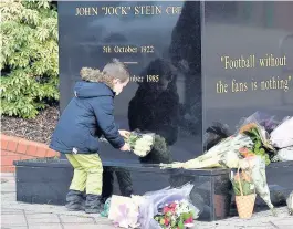  ??  ?? GENERATION­S A young Celtic fan lays down his own flowers at the statue