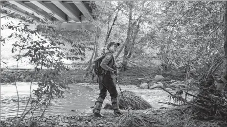  ?? ANGIE WANG/AP PHOTO ?? A Navajo County rescuer searches the riverbank under the bridge where one body was recovered in Tonto National Forest, Arizona, on Monday. Rescuers continue the search for a missing 27-year-old man, who was swept downriver with more than a dozen others...