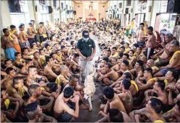  ?? AFP ?? Inmates sit on the floor of Saint Dimas chapel as Philippine Drug Enforcemen­t Agency personnel with a K9 dog look for contraband among inmates at the Manila City Jail on September 29.