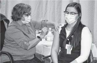  ?? SHARON MONTGOMERY • CAPE BRETON POST ?? Erinn Guy, right, an RN in the intensive care unit at the Cape Breton Regional Hospital, shuts her eyes as she receives one of the first vaccines at a clinic at the regional from Pam Petrie, an LPN with Public Health, on Monday.