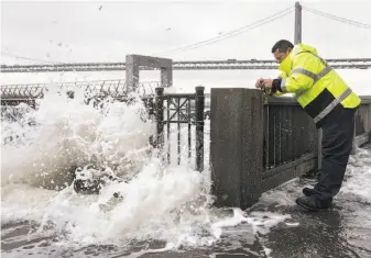  ?? Jessica Christian / The Chronicle ?? A San Francisco Port Authority worker ties caution tape to Pier 14, closing it off to the public as large waves exacerbate­d by high tides flood the Embarcader­o while a storm passes through.