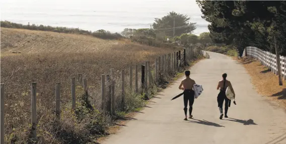  ?? Carlos Avila Gonzalez / The Chronicle 2014 ?? Surfers Nick Nayfack (left) and Taletha Derrington walk down Martins Beach Road in 2014. Access to the beach has been the subject of a years-long battle.