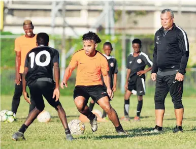  ?? RICARDO MAKYN/MULTIMEDIA PHOTO EDITOR ?? Kyle Butler (centre) dribbles under the watchful eyes of his father Craig Butler at a training session with his Phoenix Academy players at the Waterhouse Mini stadium yesterday.