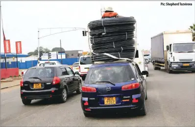  ??  ?? Pic: Shepherd Tozvireva A man rides on top of a moving vehicle while standing inside irrigation pipes in Southerton, Harare, yesterday