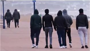  ??  ?? Out for a stroll: Migrants in groups wander along the seafront at Hythe