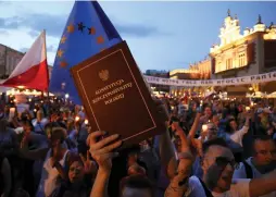  ?? (Reuters) ?? A PROTESTER HOLDS aloft a copy of the Polish constituti­on on Saturday evening during a rally in Krakow’s main square against legislatio­n aimed at controllin­g the country’s Supreme Court.