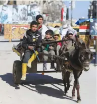  ?? (Ali Hashisho/Reuters) ?? CHILDREN RIDE a donkey cart along a street in Aleppo, Syria, as pictures of President Bashar Assad are seen in the background on February 2.