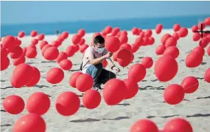  ?? SILVIA IZQUIERDO THE ASSOCIATED PRESS ?? A man helps to place red balloons in the sand on Copacabana beach on Aug. 8 in a demonstrat­ion organized by Rio de Paz to honour the victims of COVID-19.