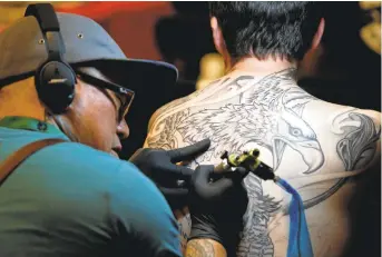  ?? ARIC CRABB/STAFF PHOTOS ?? Tattoo artist Paulo Coach Luis works on a client during the Bay Area Tattoo Convention at the Hyatt Regency in Burlingame on Sunday. “Everybody is getting them,” New York City-based artist Jon Clue said of tattoos.