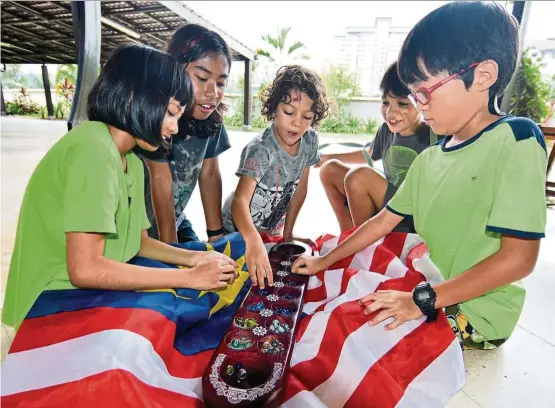  ?? — Photos: P. NATHAN/The Star ?? (Clockwise from left) Isabel, Aditya Kamiso, Zabian Omar, Malakai Omar, and Dylan Teoh learning how to play congkak.