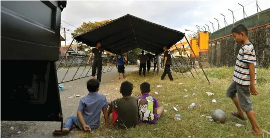  ?? ANGGER BONDAN/JAWA POS ?? SONGSONG PENENTUAN JUARA: Anak-anak menyaksika­n petugas keamanan mendirikan tenda di seputaran Stadion Andi Mattalatta, Makassar, kemarin.