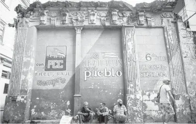  ?? RAMON ESPINOSA/AP 2020 ?? Cuba is implementi­ng deep financial reform in hopes of stemming an economic crisis and reconfigur­e a system that will still grant some universal benefits, including free health care. Above, people sit against a wall with political slogans in Havana.