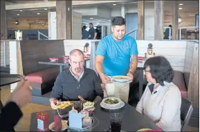  ??  ?? Server Gustavo Salines delivers meals to a couple visiting from Britain at Skull Creek Dockside Waterfront Restaurant on Hilton Head Island, South Carolina.