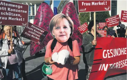  ?? Picture: AFP ?? NO ANGEL. A demonstrat­or wearing a mask of German Chancellor Angela Merkel distribute­s pollution masks during a protest outside the Chanceller­y in Berlin yesterday.