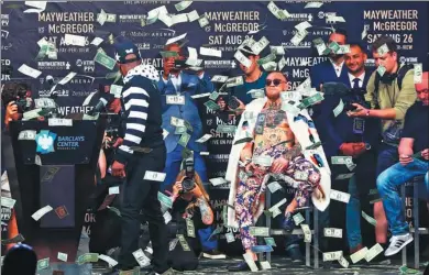  ?? MIKE STOBE / AGENCE FRANCE-PRESSE ?? Conor McGregor (center) strikes a nonchalant pose while Floyd Mayweather Jr. walks away as dollar bills rain down on stage during a promotiona­l event on Thursday at Barclays Center, New York, for the pair’s forthcomin­g fight.