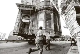  ?? Noah Berger / Associated Press ?? Workers pass a Victorian home Sunday as a truck pulls it through San Francisco. The house, built in 1882, was moved to a new location six blocks away.