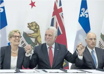  ?? JACQUES BOISSINOT/THE CANADIAN PRESS ?? Quebec Premier Philippe Couillard, flanked by Ontario Premier Kathleen Wynne, left, and California Governor Edmund G. Brown, raise their hands after signing an agreement on climate change in Quebec City on Friday.