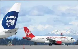  ?? Ted S. Warren Associated Press ?? A VIRGIN AMERICA plane taxis past an Alaska Airlines plane at Seattle-Tacoma Internatio­nal Airport. Alaska bought Virgin for $2.6 billion in 2016.