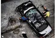  ?? NICK WAGNER / AMERICAN-STATESMAN ?? A tow truck worker releases a chain after righting the sedan that went over the edge of a downtown garage Thursday. The car breached a gas line on a building on its way down; it came to rest on its top side.