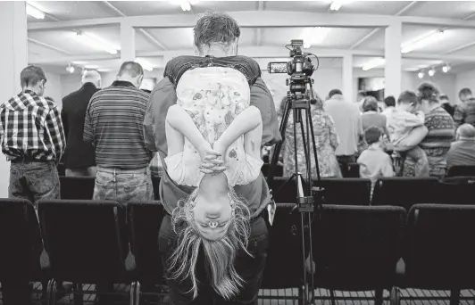  ?? Photos by Lisa Krantz / Staff photograph­er ?? John Holcombe records every service and posts the videos on YouTube. During Easter service, Evelyn prays while hanging by her knees from his shoulders.