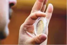  ?? AFP ?? ■ A man holds up a preserved coin specimen during an auction in Baghdad.