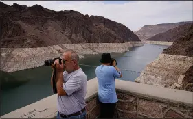  ?? JOHN LOCHER / AP FILE (2021) ?? People take pictures of Lake Mead near Hoover Dam in August 2021. The bathtub ring of light minerals shows the high water mark of the reservoir, which has fallen to record lows. Hoover Dam was built during the Great Depression in the 1930s. Workers finished pouring the concrete at Glen Canyon Dam, up-river on the Colorado in 1963. As described by Los Angeles Times columnist Michael Hiltzik, the dams and reservoirs “created only the illusion of abundant water, not the reality.”