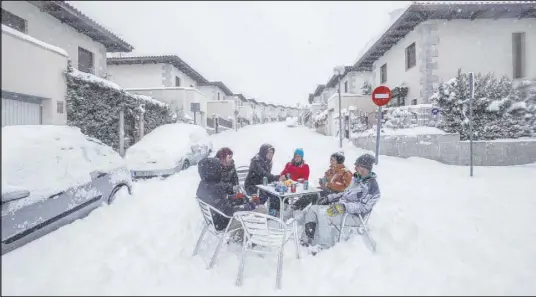  ?? Bernat Armangue The Associated Press ?? Neighbors have drinks in the street during a snowfall Saturday in Bustarviej­o, on the outskirts of Madrid.