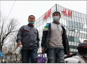  ?? (AP/Ng Han Guan) ?? Workers walk past an H&M store in Beijing on Monday, the same day the government stepped up pressure on foreign shoe and clothing brands to reject reports of abuses in the Xinjiang region.