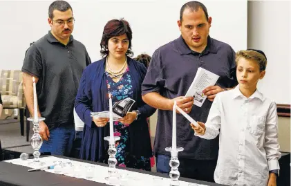  ?? STAFF PHOTO BY DOUG STRICKLAND ?? Judah Balázs, right, lights a candle with other grandchild­ren and great-grandchild­ren of Holocaust survivors during a Yom HaShoah ceremony at the Jewish Cultural Center on Wednesday. The tradition is held to honor the memories of the 6 million Jews killed during the Holocaust between 1941 and 1945.