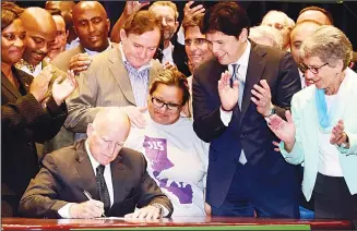  ??  ?? California Governor Jerry Brown signs the bill that will raise the state’s minimum wage to $15 an hour by 2022 while surrounded by politician­s on stage at the Ronald Reagan State Building in downtown Los Angeles on April 4.