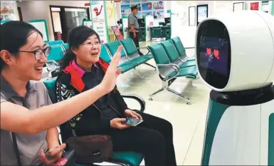  ?? WANG JILIN / FOR CHINA DAILY ?? Two women interact with a robot, which helps handle business, at an outlet of Agricultur­al Bank of China in Qingzhou, Shandong province.