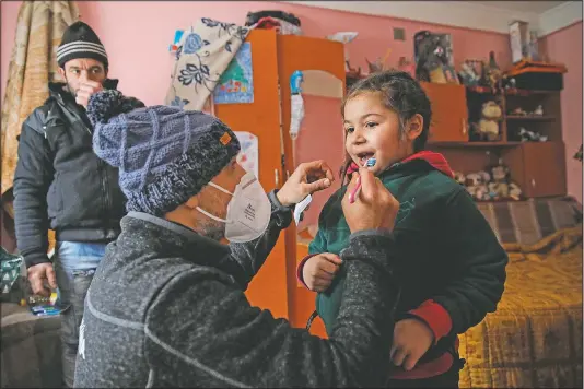  ?? (AP/Vadim Ghirda) ?? A little girl gets help from Valeriu Nicolae as she learns to brush her teeth correctly and her father watches n Nucsoara, Romania.