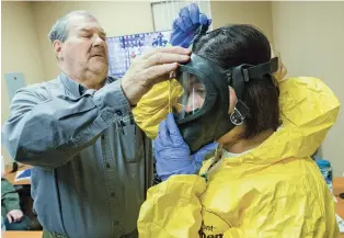  ?? LUIS SÁNCHEZ SATURNO/THE NEW MEXICAN ?? Instructor Jeffrey Biedenbach helps Aracely Tellez, an environmen­tal scientist with the state Environmen­t Department, put on her mask Friday as he conducts hazmat training.