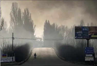  ?? ?? A man carries shopping bags as heavy smoke from a warehouse destroyed by Russian bombardmen­t casts shadows on the road outside Kyiv, Ukraine, Thursday, March 24, 2022. Ukraine President Volodymir Zelenskyy called on people worldwide to gather in public Thursday to show support for his embattled country as he prepared to address U.S. President Joe Biden and other NATO leaders gathered in Brussels on the one-month anniversar­y of the Russian invasion.