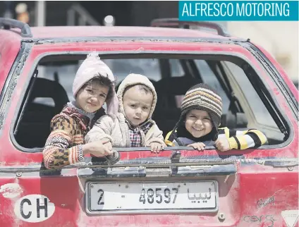  ?? Picture: Reuters ?? Children smile at passers-by from a car boot in Benghazi, Libya.