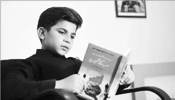  ??  ?? Hammad reads a book at his residence in Peshawar.